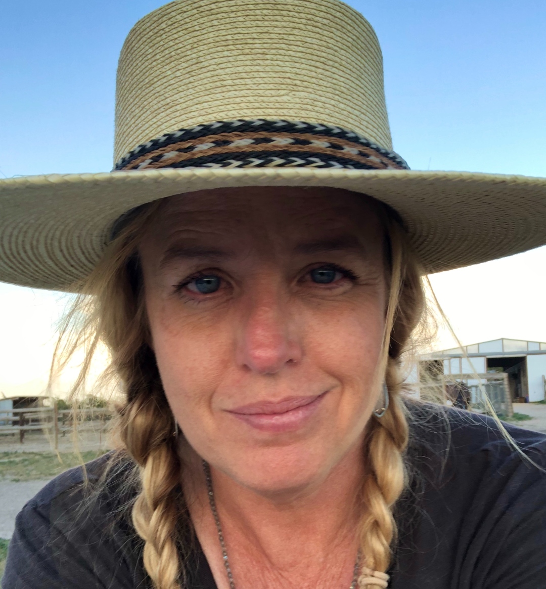 Ashley Mikel at the barn, braids and hat, looking directly at the camera
